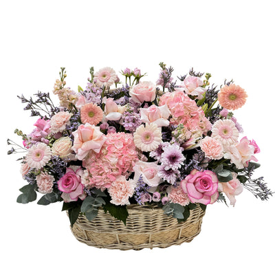 A woven basket filled with pink and purple flowers, including roses, hydrangeas, daisies, and more.