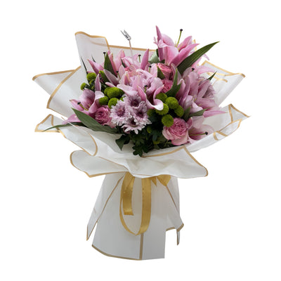 A beautiful bouquet of pink lilies, roses, and chrysanthemums wrapped in white paper with a gold ribbon.