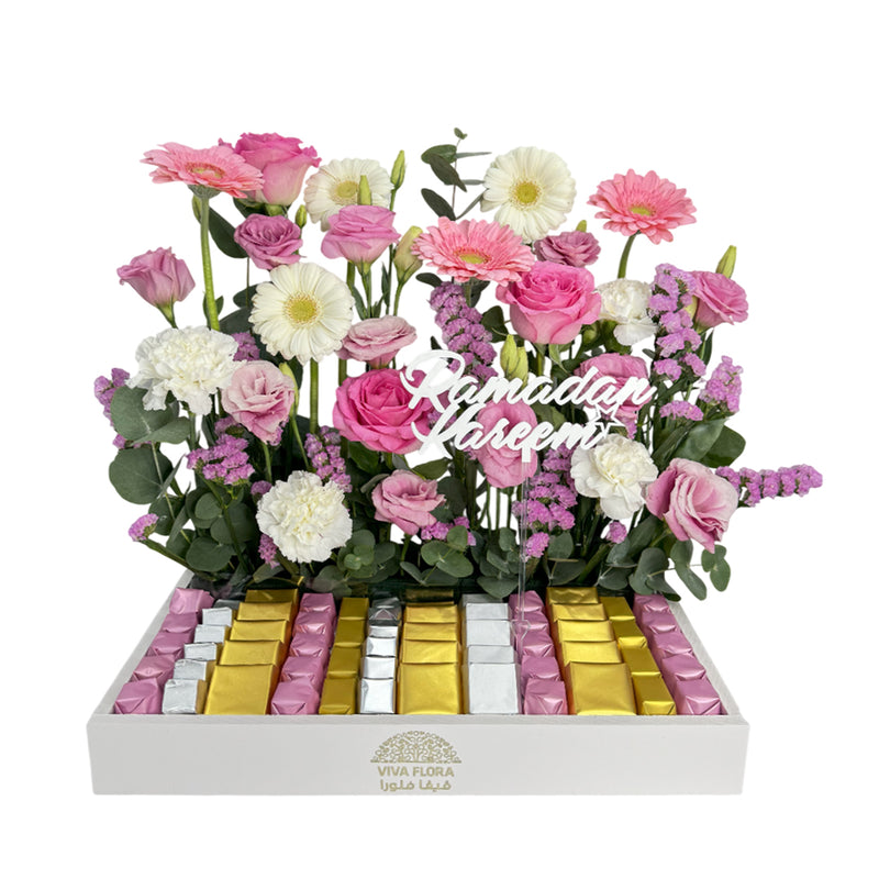 A luxurious Ramadan floral arrangement with pink and white roses, gerberas, carnations, and chocolates in gold, silver, and pink wrapping, featuring a