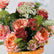 A close-up of a floral arrangement in a tan leather basket, featuring peach roses, burgundy carnations, white Queen Anne's lace, and green dill against a light background.