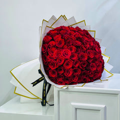Bouquet of 100 red roses wrapped in white paper with gold accents on a light gray background send the premium flowers to your loved once on qatar with viva flora 