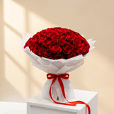 fresh 100 red roses bouquet with white wrapping displayed in a white colour podium  