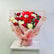 A floral gift arrangement featuring red and cream roses wrapped in pink paper with gold trim, topped with a red teddy bear, displayed on a white pedestal against a plain light gray background.