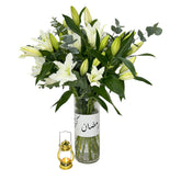  Fresh white lilies in a glass vase with lush greenery and a decorative lantern near by.