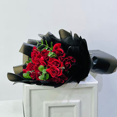 budget friendly flower bouquet for valentines day, Bouquet of red roses wrapped in black paper on a white surface with a light gray background