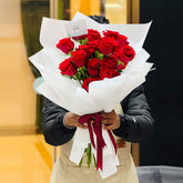Person holding a bouquet of red roses wrapped in white paper with a red ribbon. especially made for valentines day 2026 