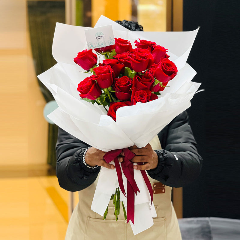 Person holding a bouquet of red roses wrapped in white paper with a red ribbon. especially made for valentines day 2026 