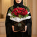 A bouquet of red roses wrapped in white tissue paper and presented in a black square box with the brand name VIVA FLORA, placed on a white cylindrical pedestal against a beige wall with soft window shadows.