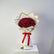 A bouquet of red roses wrapped in white paper with gold trim and a red ribbon, displayed on a white box against a light gray background.