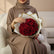 A bouquet of 20 red roses wrapped in white paper with gold trim and tied with a red ribbon, displayed on a white pedestal against a beige background.