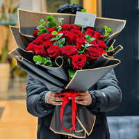 Bouquet of red roses wrapped in black paper with a red ribbon held by a person.