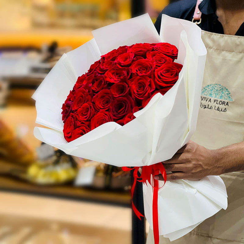 Bouquet of red roses made for valentine new collections held by a person wearing a 'Viva Flora' apron.