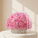 A large round arrangement of pink roses in a white wicker basket, tied with a pale pink ribbon, set on a marble surface in a softly lit indoor room.