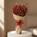 A person wearing a black abaya holds a large bouquet of red roses wrapped in brown paper with a red ribbon, set against a softly lit beige indoor background.