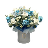 A beautiful blue and white floral arrangement in a hatbox with a "Baby Boy" topper, perfect for welcoming a newborn.
