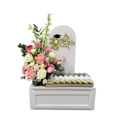 Graduation gift arrangement with fresh roses and assorted chocolates in a white box, featuring 2025 topper and Arabic calligraphy.