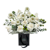  A black gift bag filled with white roses, daisies, and eucalyptus leaves.