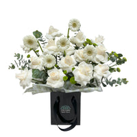  A black gift bag filled with white roses, daisies, and eucalyptus leaves.