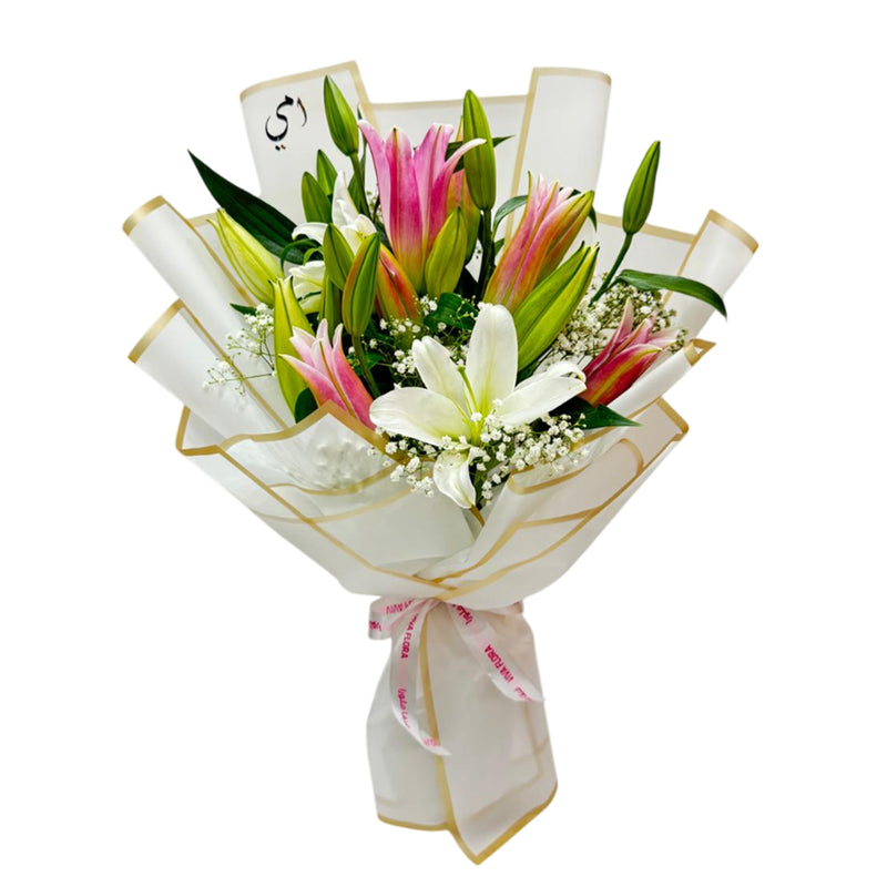 Bouquet of pink and white lilies wrapped in white and gold tied with a ribbon at the bottom placed on the table. 