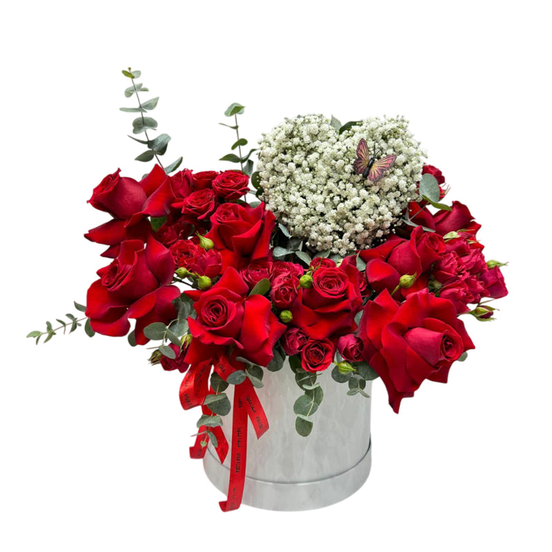 A white flower box with red roses, heart shaped gypso, eucalyptus accented by a butterfly.