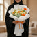 A Father's Day flower bouquet wrapped in white tissue paper and tied with an orange ribbon, featuring orange and white flowers with green foliage and a 'Happy Father's Day' card.