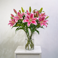 A bouquet of pink and white striped lilies in a clear glass vase, placed on a white side table against a light gray wall.