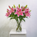 A bouquet of pink and white striped lilies in a clear glass vase, placed on a white side table against a light gray wall.