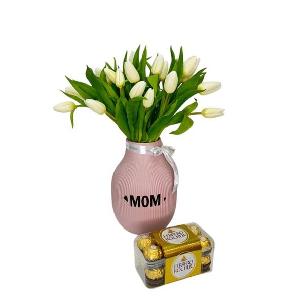 White tulips in pink "MOM" vase with chocolates on white table