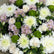 A large floral arrangement of white and pale pink flowers with green accents, wrapped in beige paper and displayed on a light gray floor.