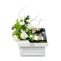 White floral gift box with peach-toned roses, gerberas, and 800g of assorted chocolates, tied with black ribbon—presented in a Viva Flora tray.