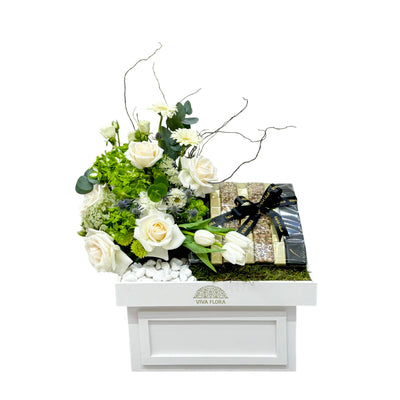 White floral gift box with peach-toned roses, gerberas, and 800g of assorted chocolates, tied with black ribbon—presented in a Viva Flora tray.