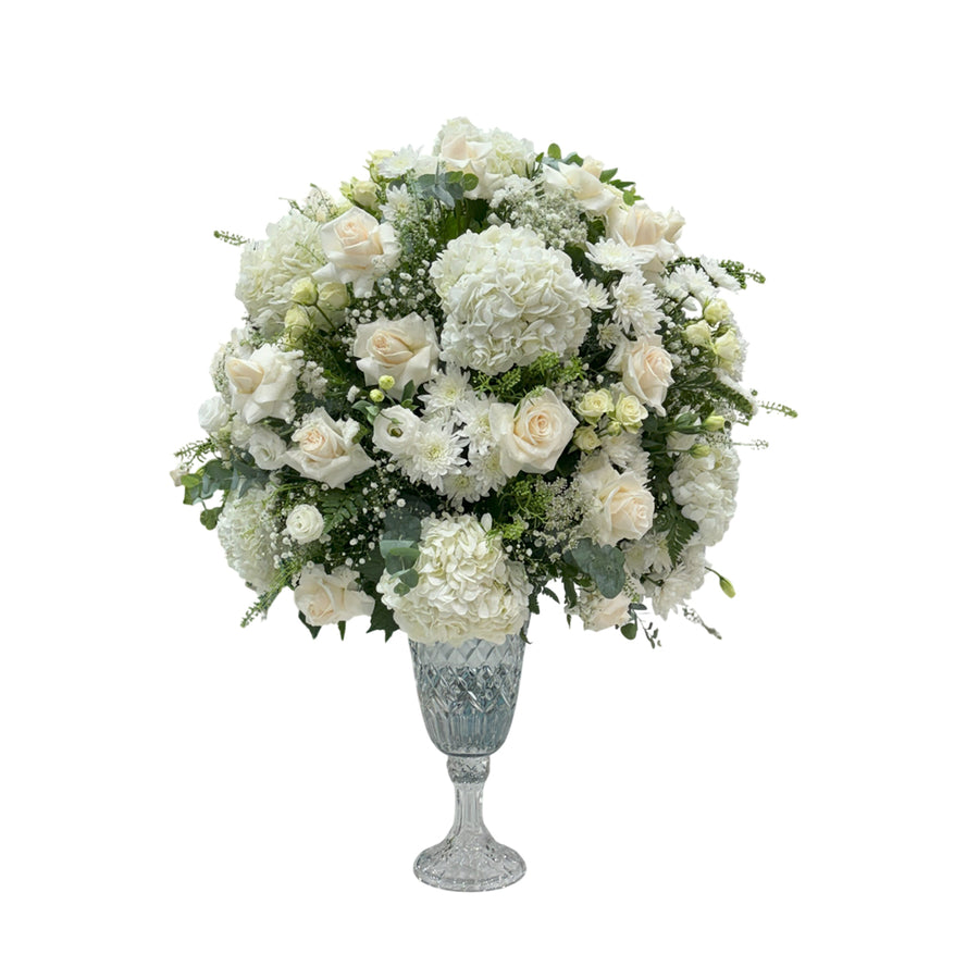 An elegant white bouquet of roses, hydrangeas, and chrysanthemums in a crystal vase.