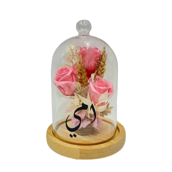 Preserved pink roses in a glass dome with a wooden base.