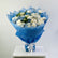 A bouquet of white roses, blue baby's breath, and green foliage wrapped in bright blue tissue paper and tied with a white ribbon, displayed on a white pedestal against a light gray background.