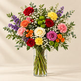 A colorful bouquet of artificial flowers wrapped in brown kraft paper and a white ribbon, placed on a white marble-patterned surface.