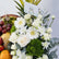 A close-up of a floral arrangement featuring white roses, daisies, eucalyptus leaves, and green moss, with a small card holder displaying 'VIVA FLORIDA' and fruit arranged around it.