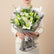 A bouquet of white lilies and green buds wrapped in gray paper with a white ribbon, displayed on a white pedestal against a warm beige background.