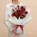 A bouquet of red roses wrapped in white tissue paper with a red ribbon and a white script 'Love' sign, displayed on a white pedestal against a warm beige background.