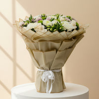 A large floral bouquet wrapped in beige paper and tied with a white ribbon, displayed indoors on a White Podium and badge colour background  