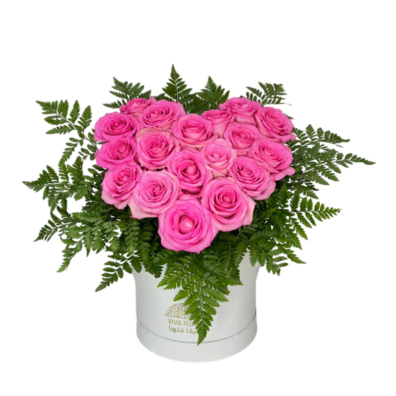 Heart-shaped pink rose arrangement with lush green foliage in a white floral box.