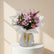 A beautiful bouquet of pink lilies, roses, and chrysanthemums wrapped in white paper with a gold ribbon.
