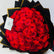 A large bouquet of vibrant red roses wrapped in black paper with gold edges, featuring a small white card with a floral illustration and the text 'THE PERFECT GIFT'.