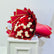 A large bouquet of red and white roses wrapped in red paper with gold edges, displayed on a white pedestal against a plain light background.
