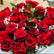 A large bouquet of deep red roses with green leaves and small white baby's breath, wrapped in white tissue paper and clear cellophane, held in front of a shop window.