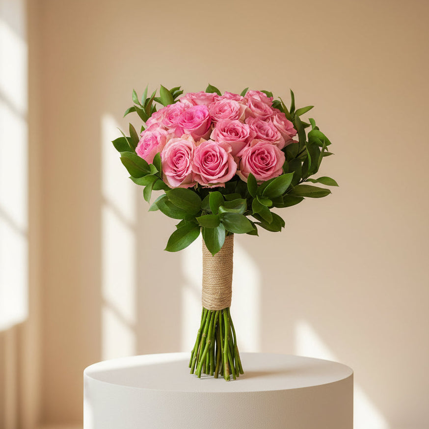 A person wearing a black abaya and headscarf holds a large bouquet of pink roses with green leaves, wrapped in twine at the stem, against a softly blurred indoor background.