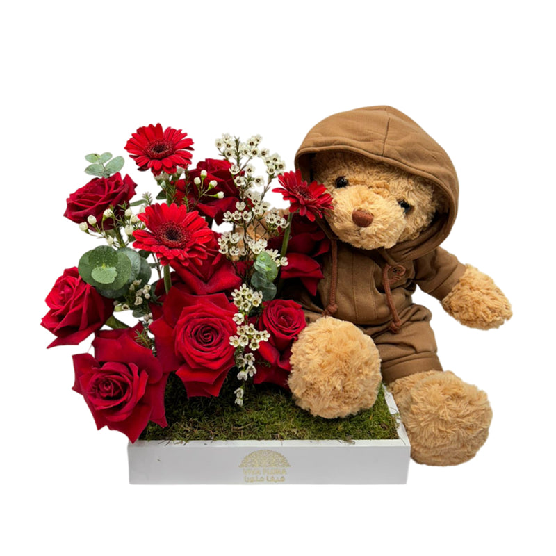 A stunning arrangement of red roses, gypso, and greenery, complemented with a cuddly teddy bear.