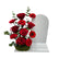 An arrangement of  deep red roses, carnations, and greenery with a white board on the right.