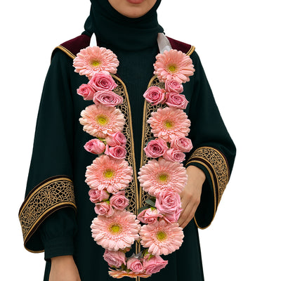 Pink gerbera and rose floral garland necklace on a female graduate in black and gold gown