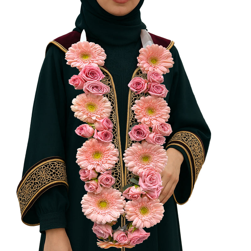 Pink gerbera and rose floral garland necklace on a female graduate in black and gold gown