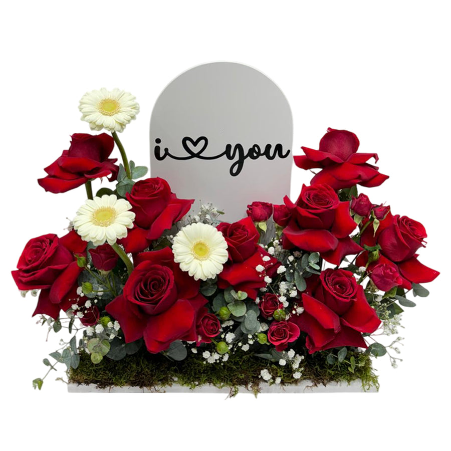 Flower arrangement with red roses, white gerberas, with  "I Love You" sign in middle.